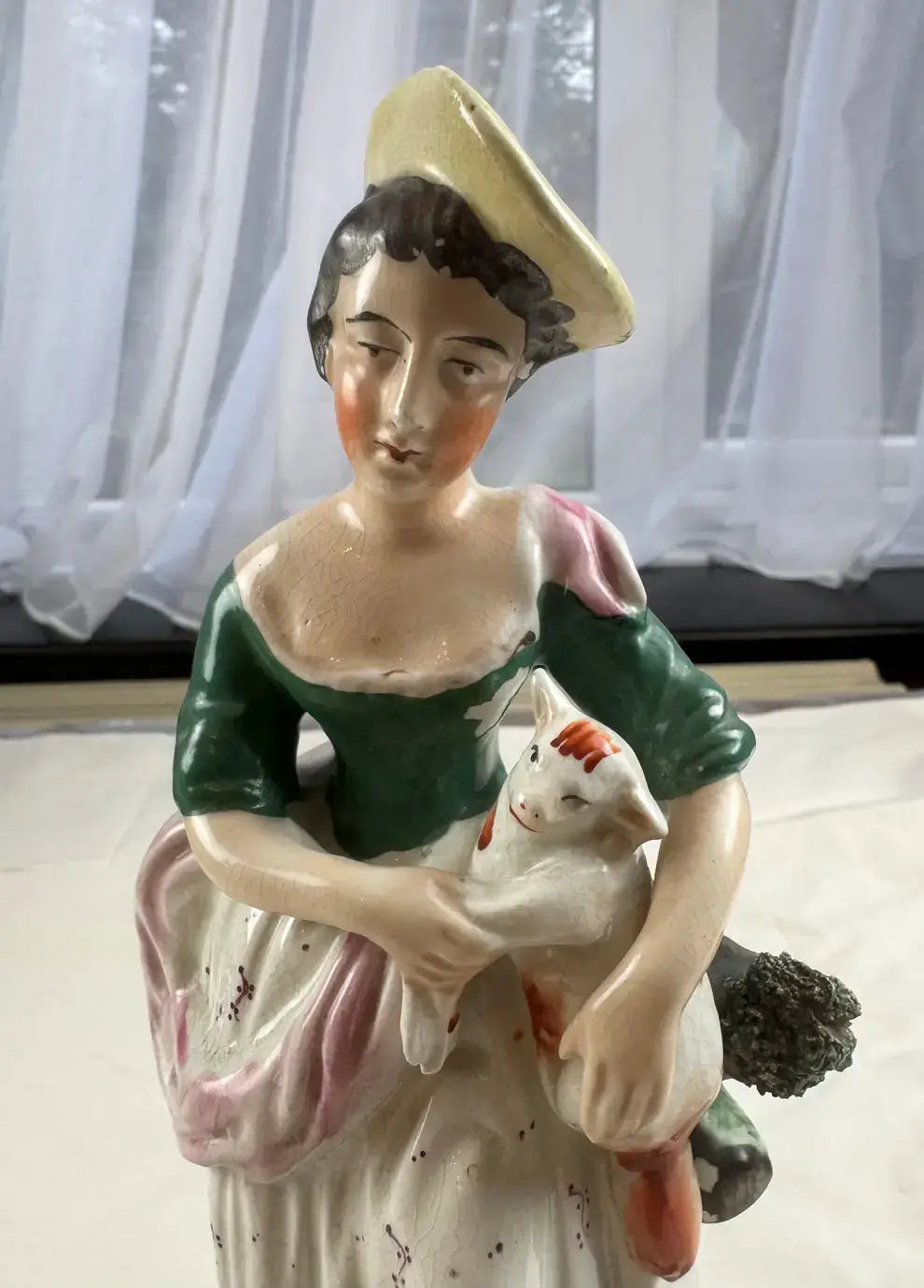Exquisite 19th century Staffordshire figurine of a woman in yellow bonnet cradling a white-and-ginger cat amid lush greenery.