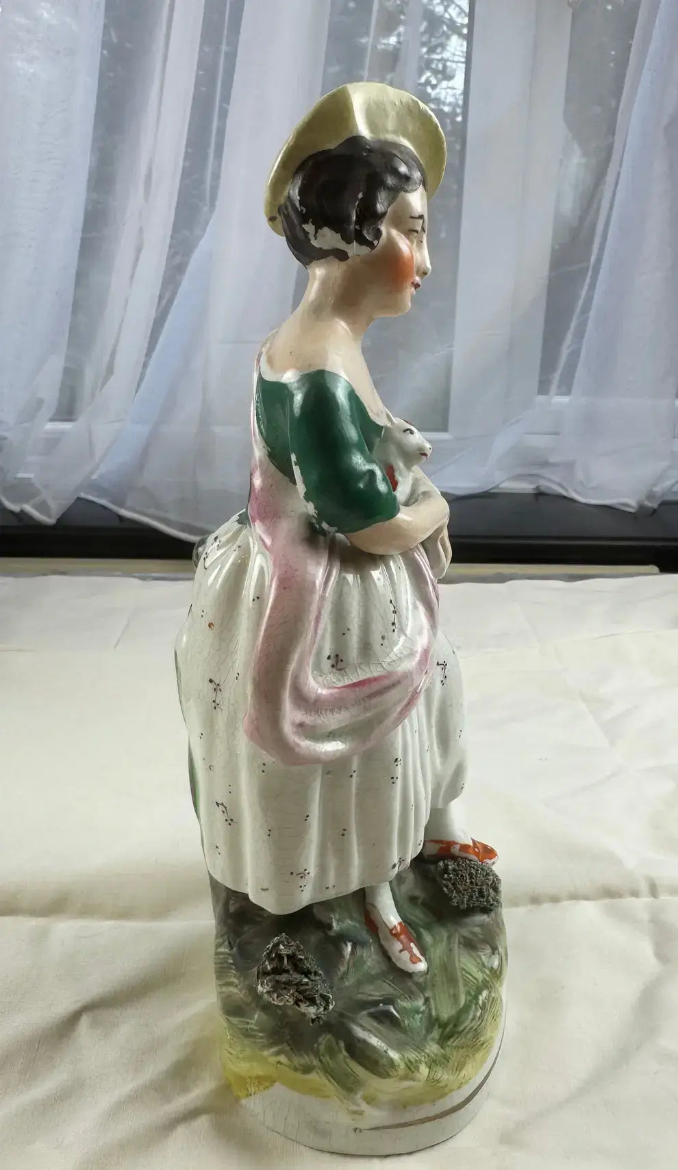 Exquisite mid-19th-century Staffordshire figurine of a woman in a yellow bonnet cradling a cat among greenery.